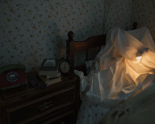 A bedside table lamp emitting warm yellow light next to a book on a clean sheet